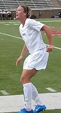 Wambach wearing a white uniform by a soccer field.