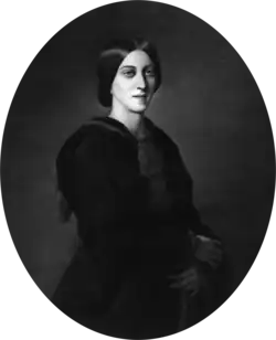 Three-quarter oval portrait of a slender woman aged about 30, garbed in black. Her deep-set eyes gaze solemnly over the viewer's shoulder. Her dark, straight hair is parted in the centre and pulled back in a low bun.