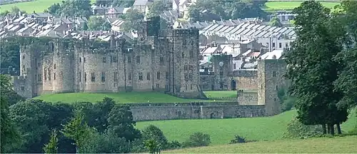 A large castle, with a ditch and trees in front of it.