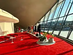 The Ambassador Club, a space on the upper level with a red carpet and a slanting glass wall under a sloped concrete ceiling.