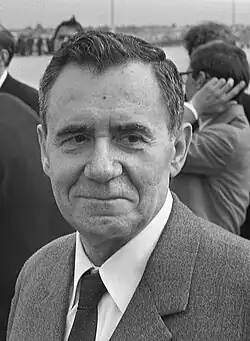A man in a dark suit, seated, looking to his left