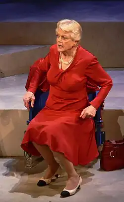 An elderly white woman wearing a red dress sitting in a chair