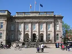 A grand Palladian building on the opposite side of a square. It is designed like the portico of a massive building with pillars in front of and between the windows, but has no extension to either side, being rather cubic in shape.