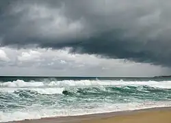 A beach is battered by choppy seas from an offshore storm and overcast, dark skies hang overhead.
