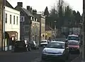 Street scene showing brown stone houses with tiled roofs. Several parked cars in the road.