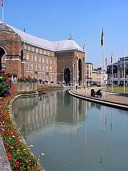 A large brick building, built in a shallow curve, with a central porch. In front of that is a pool and a water fountain.