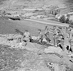 Six men around an artillery gun dug in with another gun in the distance