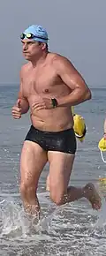 A man running in the ocean with square cut swim trunks