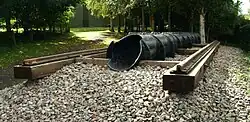 Exterior in woodland. a short section of railway line on wooden sleepers with a cast iron pipe of approximately one foot diameter, running inline with the rails