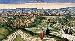 Dozens of houses and churches surrounded by a wall with bastions, with mountains in the background
