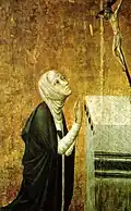 St. Catherine of Siena, wearing a white veil and black mantle, kneels in prayer before an altar with a crucifix.