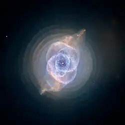 Blue-green diffuse disk with complex circular structure in its center. The disk is crossed by s-shaped brown curve.
