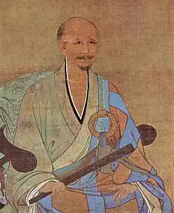 A portrait of an older, balding man in a half pale green and half sky blue robe. He is sitting on an armchair holding a thin wooden stick, possibly a folded up fan.