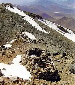 Squat ruined buildings on a mountain slope with snowy patches