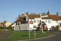 Road junction with direction sign. In the background is a white painted building with a pub sign saying The Crown.