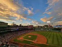 Baseball stadium at sunset with a game in progress and floodlights illuminating the field