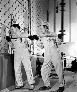 Two workmen in overalls put a rod into a hole on the reactor face