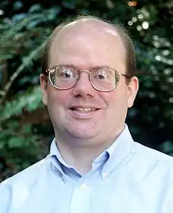 Headshot of a bespectacled balding man in a light blue shirt facing the camera.