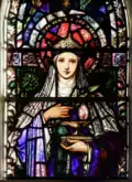St. Brigid holds a golden lamp with a perpetual flame, and a sprig of oak leaves