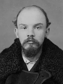 A mugshot of a young balding man with a Van Dyke beard.