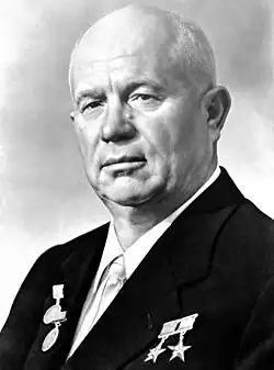 An elderly bald man in a suit, with several medals pinned on it