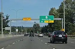 A four-lane freeway separated from oncoming traffic by a concrete barrier. A sign in the background indicates that the exit for State Route 202 is approaching.