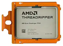 Gray packaged IC in orange carrier frame on white background labeled with AMD logo, AMD Ryzen Threadripper 7970X and 2022 copyright
