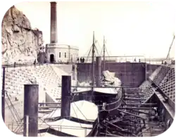 A photograph with two steamships resting in a dewatered drydock with a building housing the engine for operating the lock's gates in the background