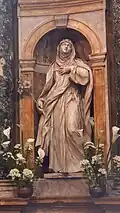 St. Catherine of Siena, wearing a mantle and veil, a crown of thorns upon her head, holds a stalk of lilies.