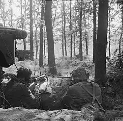 Two men facing away from the camera armed with Sten guns