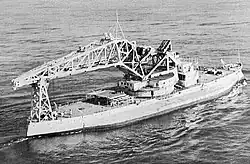 Kearsarge with a large crane on her deck. The crane is approximately half the ship's length and is mounted at the center of the ship on a turntable that is as wide as the upper deck.