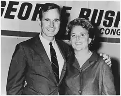 George and Barbara stand in front of a George Bush for Congress sign. George's arm is around Barbara's shoulders.