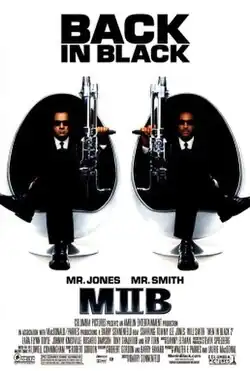 Two men in black men, sitting in egg-shaped chairs, holding large guns