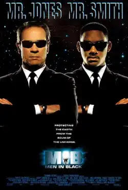 Two gentlemen, both wearing suits and sunglasses, a Caucasian and an African-American, are faced toward the viewer.